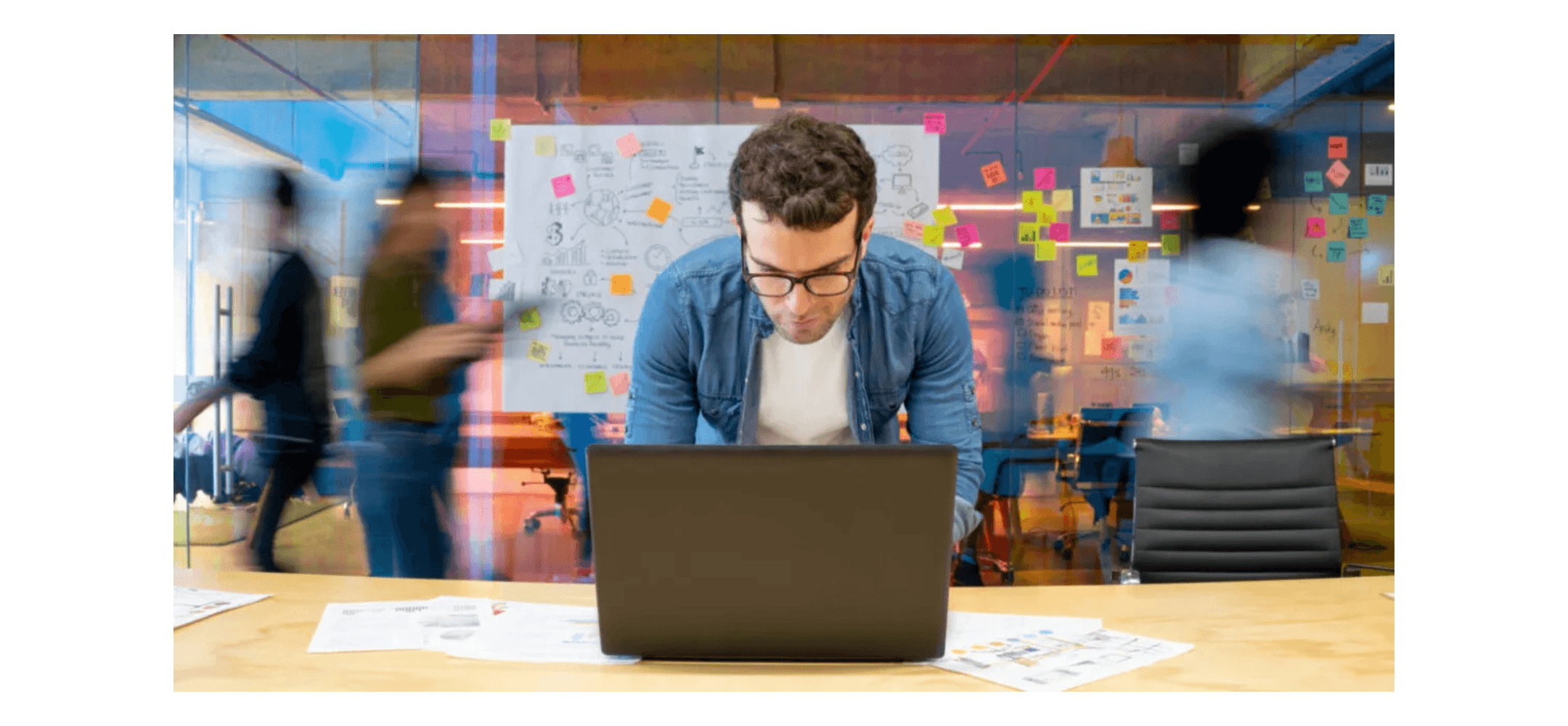Man met bril werkt geconcentreerd op een laptop in een dynamische kantooromgeving met post-its op de muur